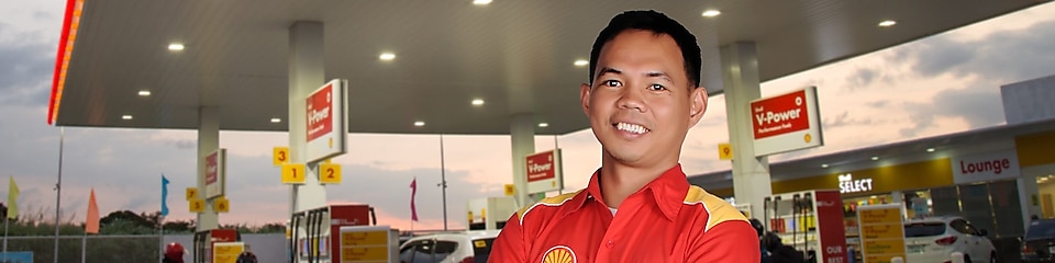 man standing in front of Shell station with folded hands and smiling